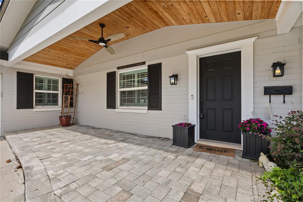 A covered front porch with a wood-paneled ceiling, paver flooring, and a black front door — 703 NICOMA TRAIL, MAITLAND, FL