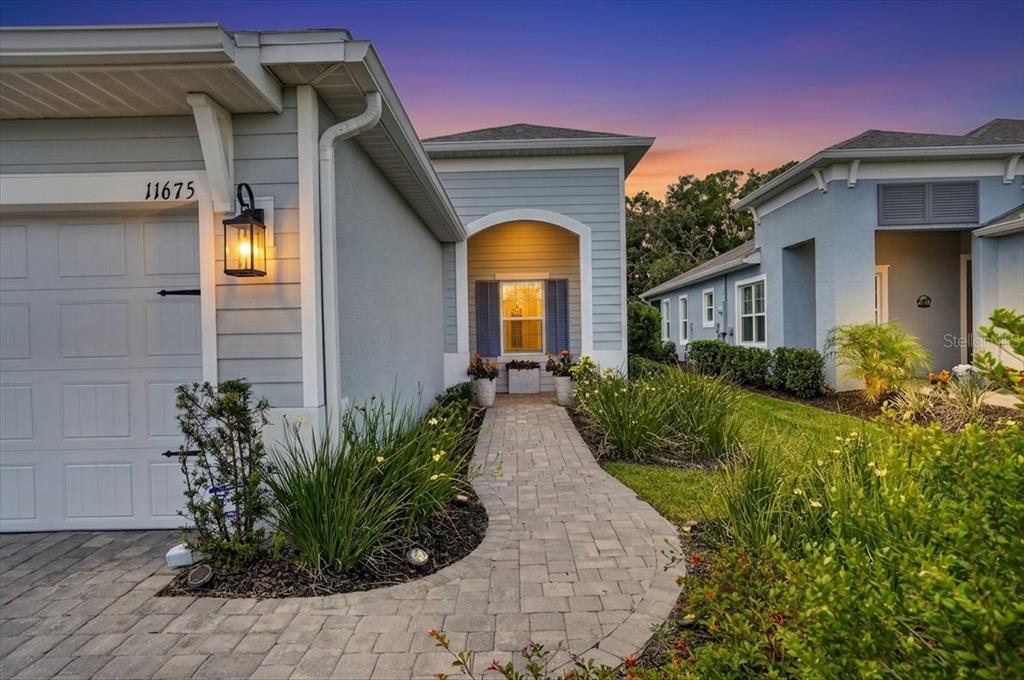 A paved walkway leads to the entrance of a light blue house with a garage — 11675 GREAT BROOK LANE, PARRISH, FL