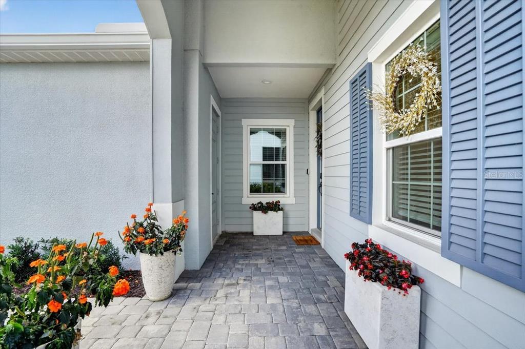 A covered entryway features gray siding, blue shutters, a stone-paver floor, and potted plants — 11675 GREAT BROOK LANE, PARRISH, FL
