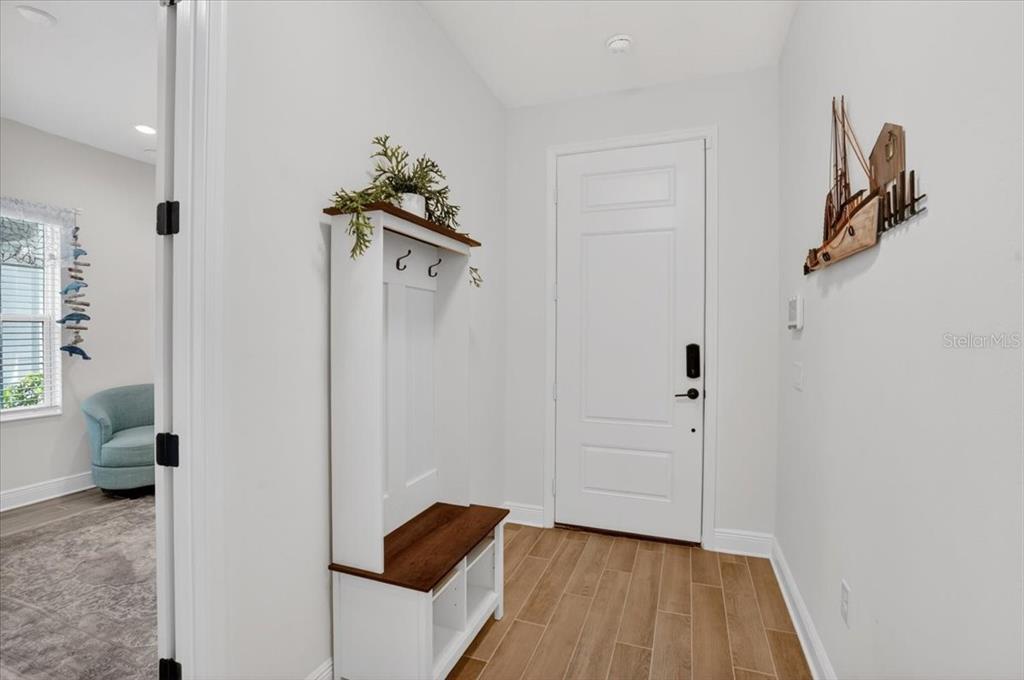 An entryway features a white door, a wooden coat rack bench, and light wood-look flooring — 11675 GREAT BROOK LANE, PARRISH, FL