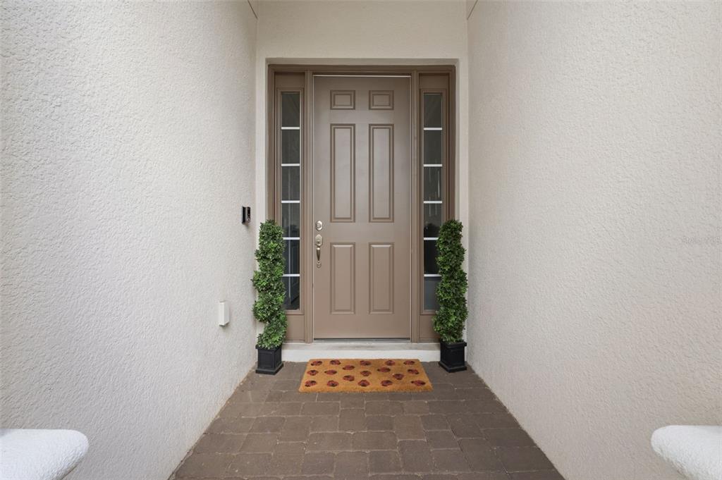 A front entryway features a tan door with sidelights, two potted topiaries, and paver flooring — 9750 HIGHLAND PARK PLACE, PALMETTO, FL
