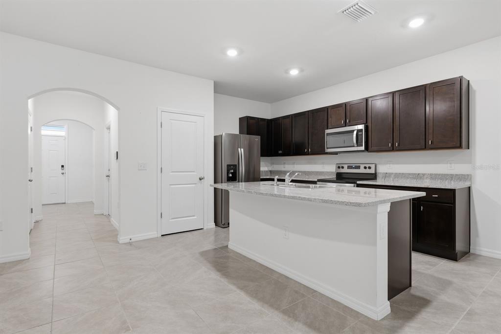 A kitchen with dark wood cabinets, granite countertops, a center island, and light tile flooring — 13753 NW 9TH ROAD, NEWBERRY, FL