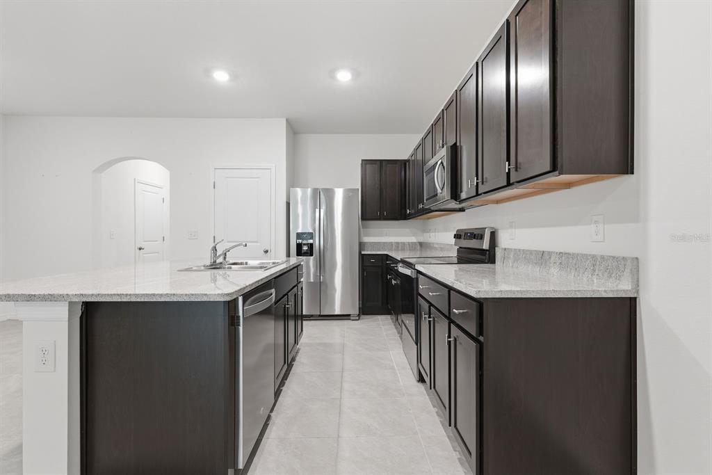 A kitchen features dark wood cabinets, granite countertops, stainless steel appliances, and a central island — 13753 NW 9TH ROAD, NEWBERRY, FL