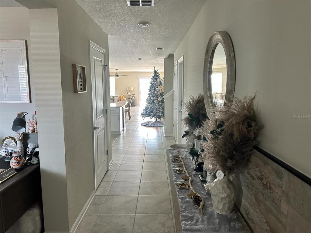 A tiled hallway leads past a console table and mirror toward a kitchen and Christmas tree — 4499 MAGNOLIA RIDGE COURT, KISSIMMEE, FL