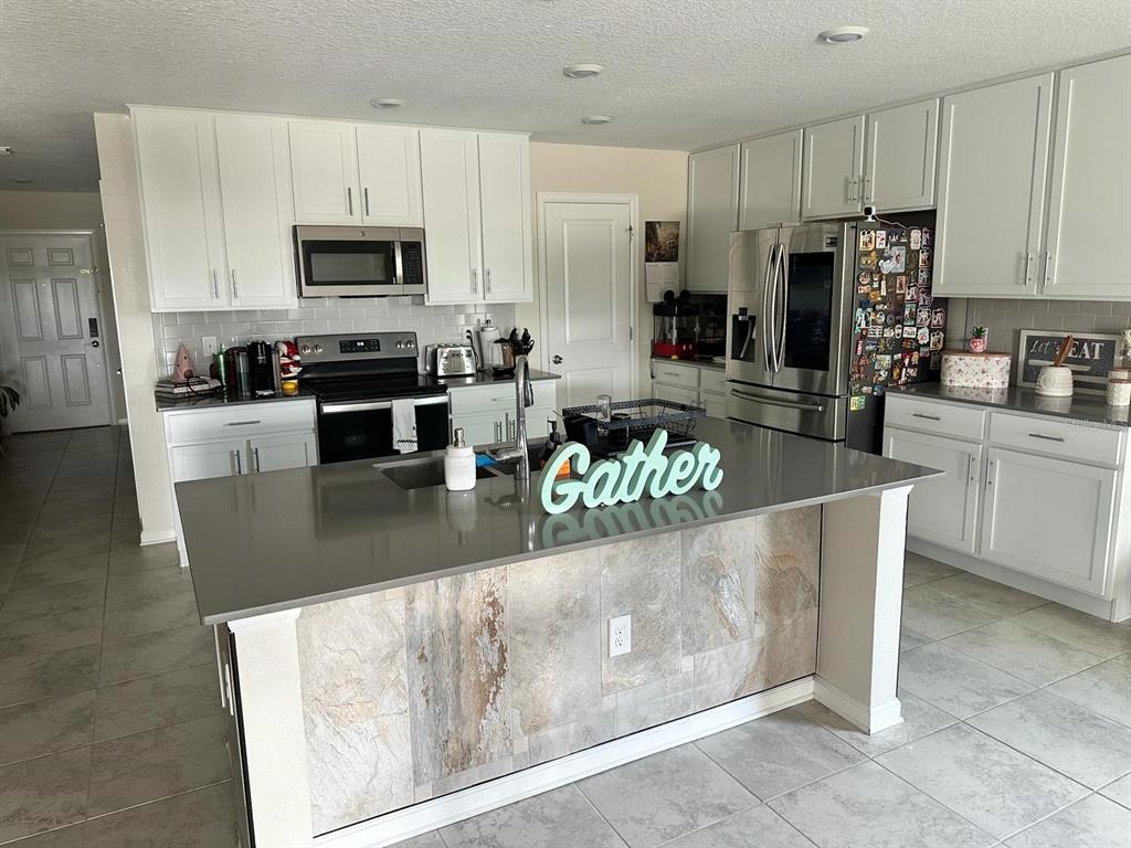 A kitchen features white cabinets, stainless steel appliances, a tiled island, and gray countertops — 4499 MAGNOLIA RIDGE COURT, KISSIMMEE, FL