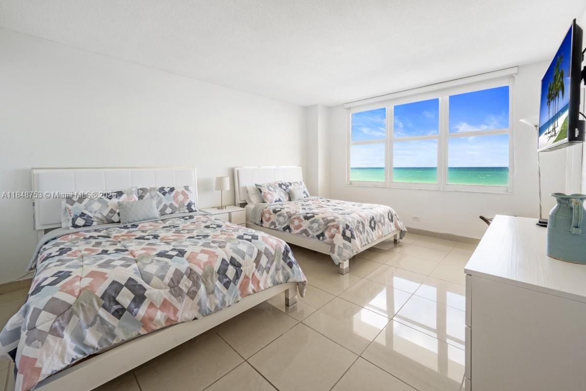 A bedroom with two beds, tile floors, and a large window overlooking the ocean — 5601 Collins Ave # 511, Miami Beach FL 33140, MIAMI BEACH, FL