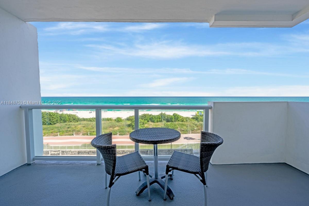 A balcony with a small table and two chairs overlooks the beach and ocean — 5601 Collins Ave # 511, Miami Beach FL 33140, MIAMI BEACH, FL