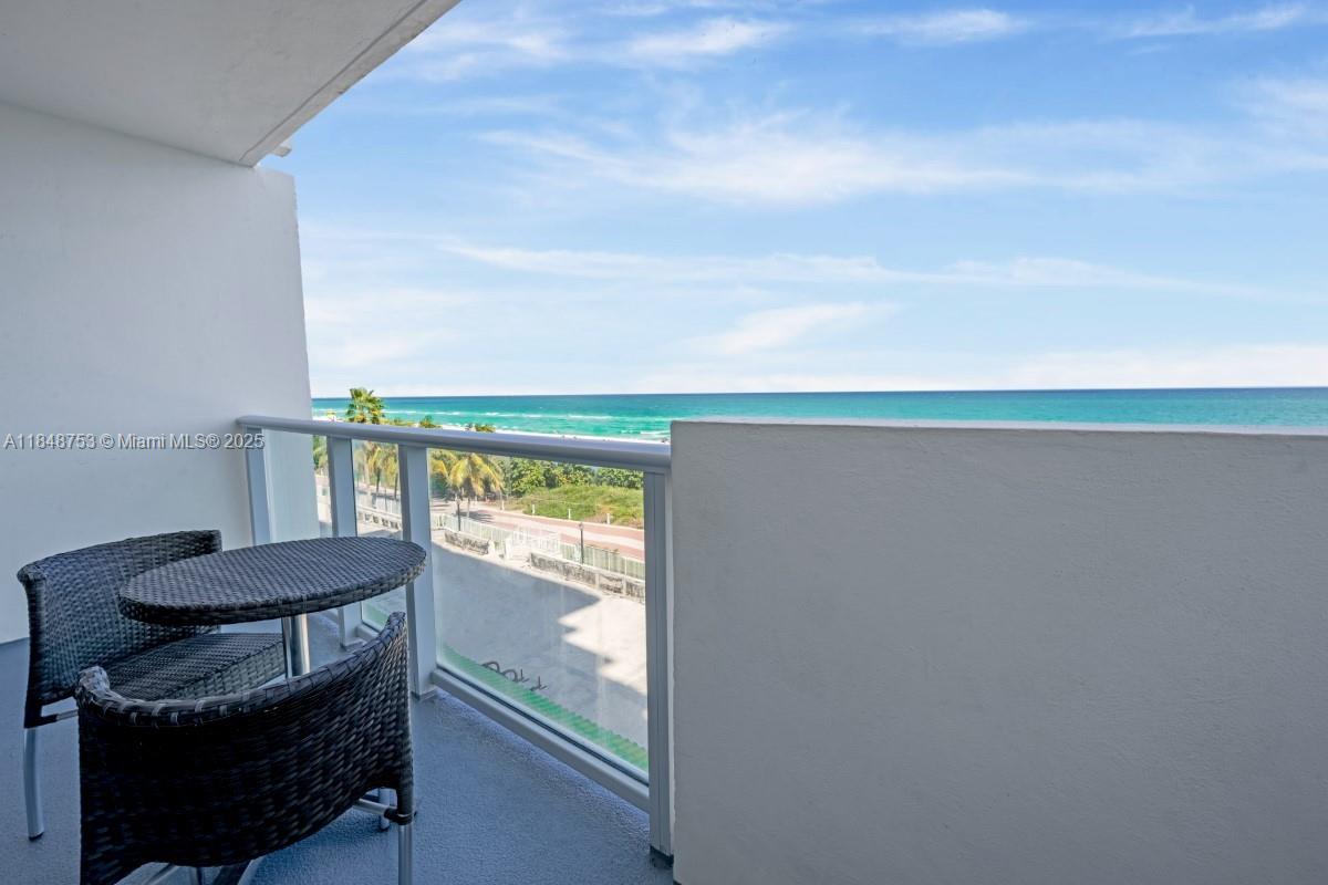 A balcony with a small table and two chairs overlooks the ocean and beach — 5601 Collins Ave # 511, Miami Beach FL 33140, MIAMI BEACH, FL