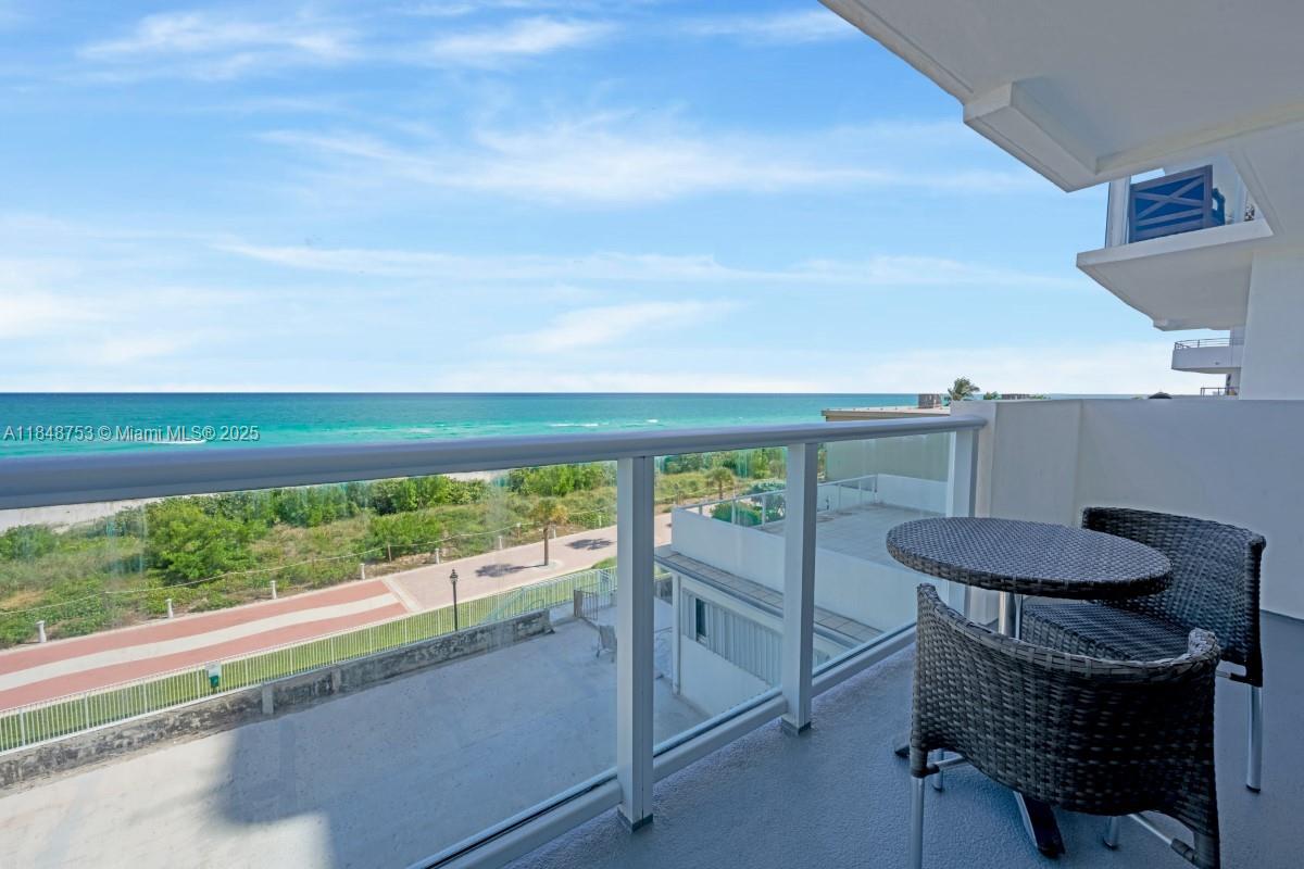 A balcony with wicker furniture overlooks a beach, a paved path, and the ocean — 5601 Collins Ave # 511, Miami Beach FL 33140, MIAMI BEACH, FL