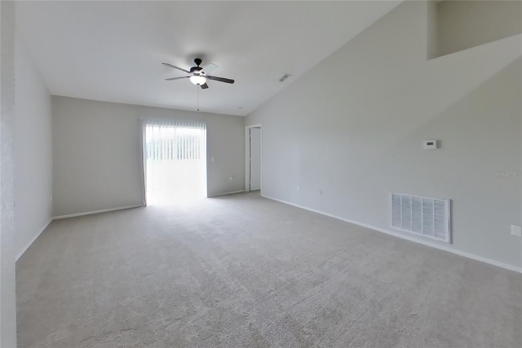 An empty living room features beige carpeting, light gray walls, a vaulted ceiling, and sliding doors — 3034 WENTWORTH PLACE, LAKELAND, FL