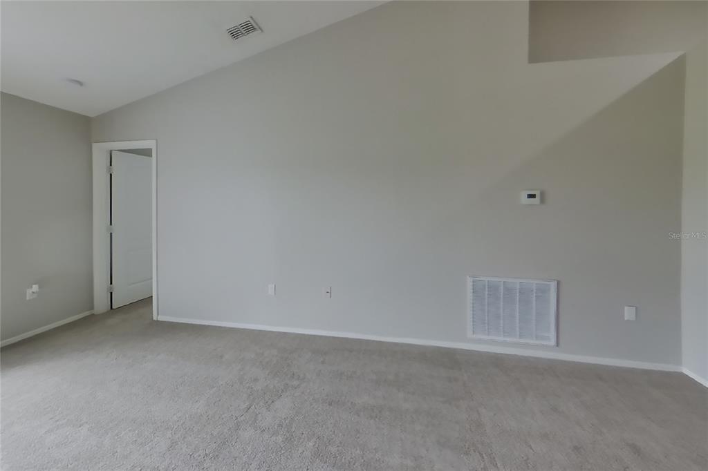 An empty room features gray walls, beige carpeting, a vaulted ceiling, and a white door — 3034 WENTWORTH PLACE, LAKELAND, FL