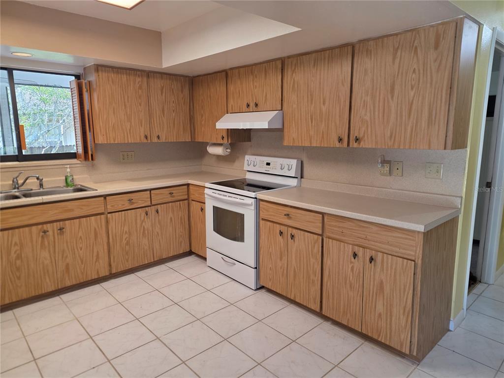 A kitchen features wood cabinets, white appliances, tile flooring, and a window above the sink — 4841 SUNDAY COURT, SARASOTA, FL