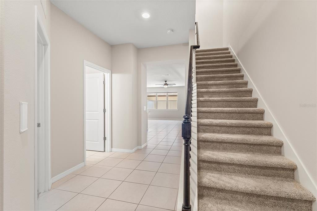 A tiled entryway features a carpeted staircase with a dark metal railing and a doorway — 5046 WALKER STREET, ST CLOUD, FL