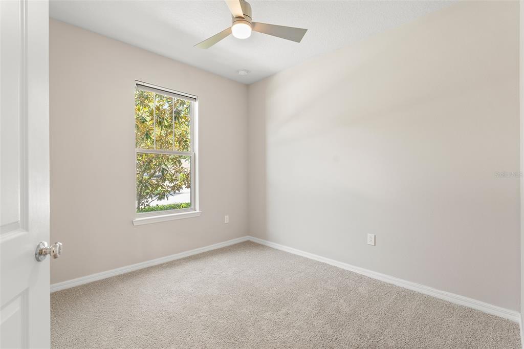 An empty bedroom features beige walls, neutral carpeting, a ceiling fan, and a single window — 5046 WALKER STREET, ST CLOUD, FL