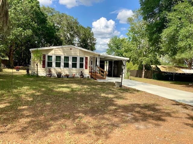 A light-colored single-story house with a covered porch and a concrete driveway — 13957 COUNTY ROAD 109D, LADY LAKE, FL
