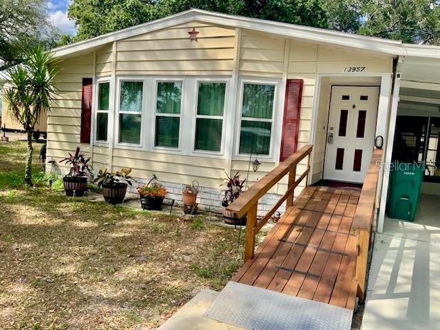 The exterior of a light-colored mobile home features red shutters and a wooden wheelchair ramp — 13957 COUNTY ROAD 109D, LADY LAKE, FL