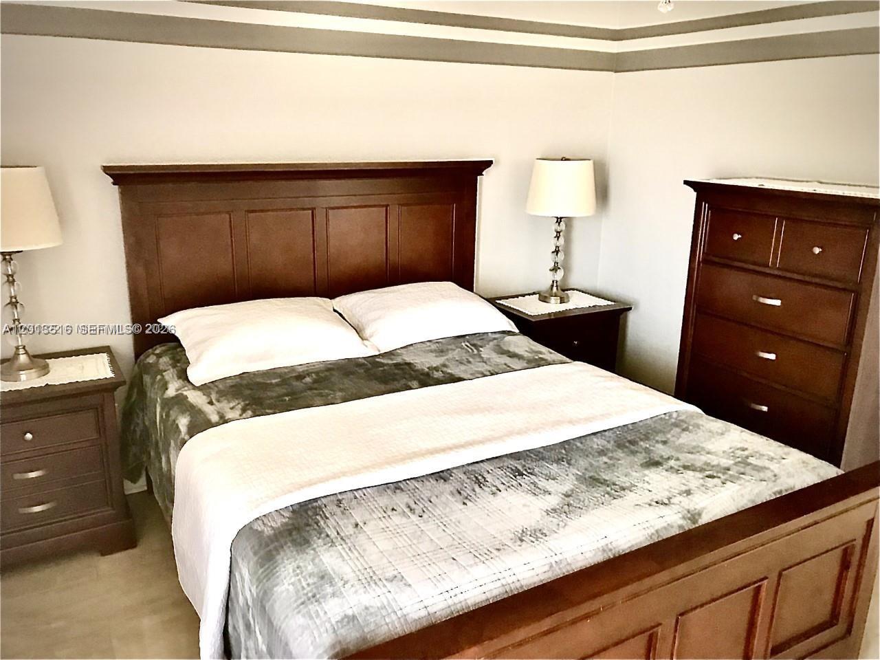 A bedroom features a wooden bed frame, two nightstands with lamps, and a tall dresser — 900 SW 11th Ave # 17C, Hallandale Beach FL 33009, HALLANDALE BEACH, FL
