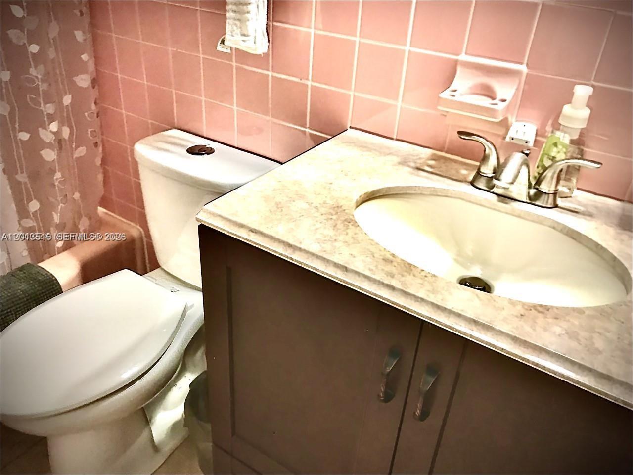 A bathroom features a vanity with a stone countertop, a toilet, and pink wall tiles — 900 SW 11th Ave # 17C, Hallandale Beach FL 33009, HALLANDALE BEACH, FL