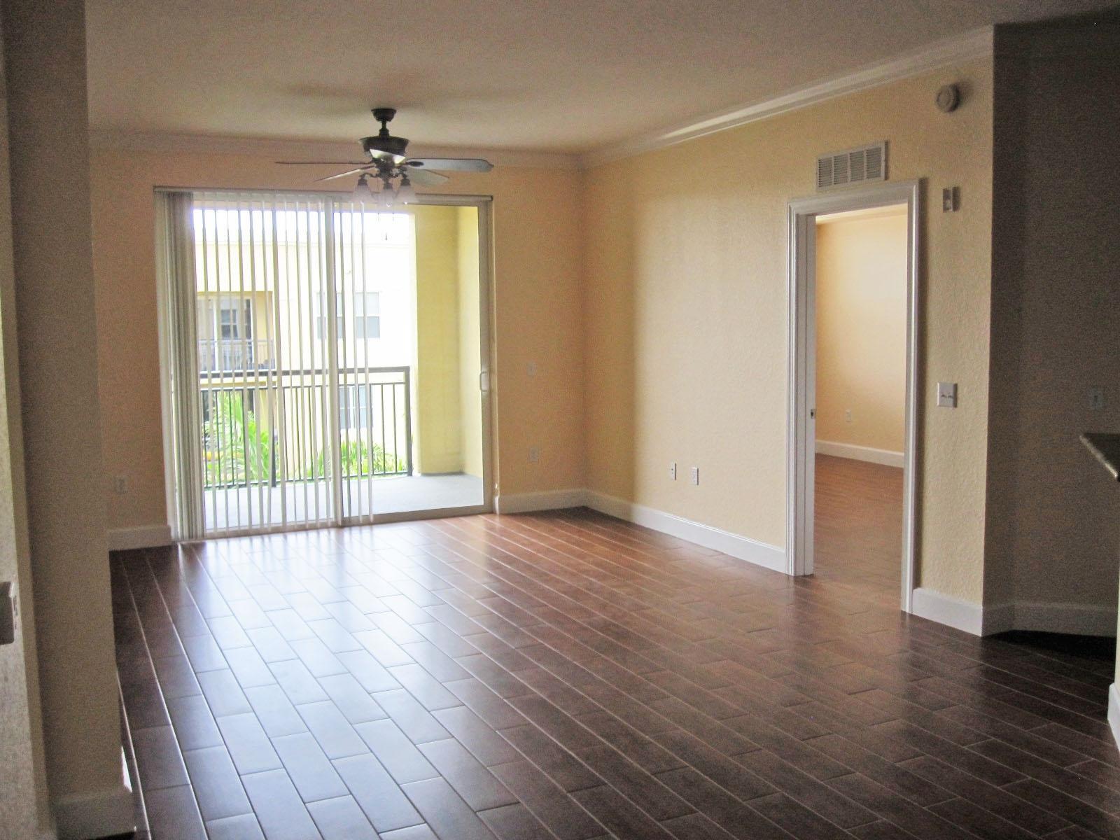 An empty living room with dark wood-look tile flooring, a ceiling fan, and sliding doors — 1690 Renaissance Commons Boulevard # 1629, Boynton Beach FL 33426, BOYNTON BEACH, FL