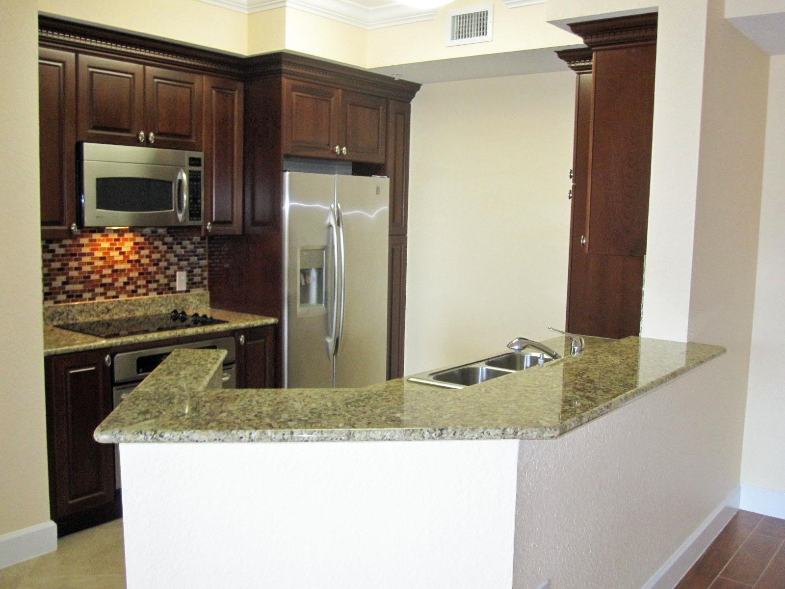 A kitchen features dark wood cabinets, granite countertops, stainless steel appliances, and a breakfast bar — 1690 Renaissance Commons Boulevard # 1629, Boynton Beach FL 33426, BOYNTON BEACH, FL