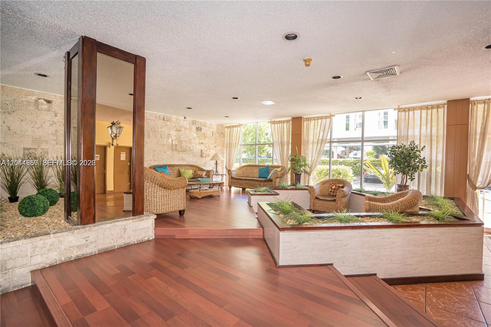 A lobby features wood flooring, stone walls, wicker furniture, and built-in planters with greenery — HIALEAH, FL