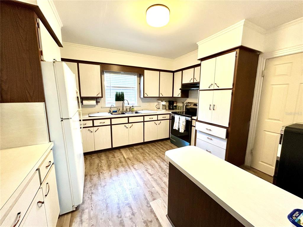 A kitchen features white cabinets with dark wood trim, light wood-look flooring, and white appliances — 265 W BAY AVENUE, LONGWOOD, FL