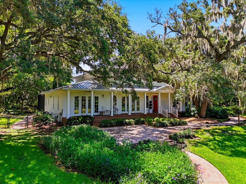 A white house with a metal roof and a front porch sits under large oak trees — 1645 CRUMP ROAD, WINTER HAVEN, FL
