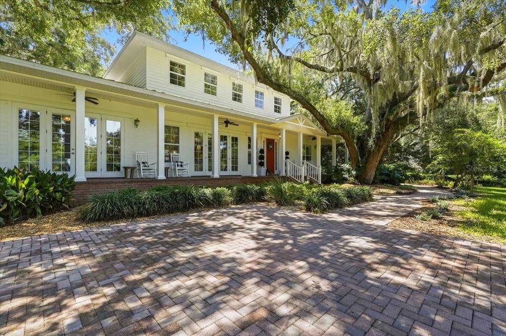 A white two-story house with a brick porch and large oak trees in the yard — 1645 CRUMP ROAD, WINTER HAVEN, FL