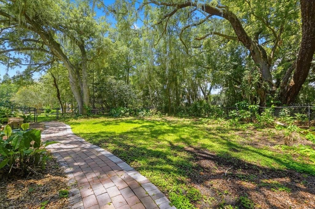 A brick walkway leads through a grassy backyard surrounded by large, moss-draped oak trees — 1645 CRUMP ROAD, WINTER HAVEN, FL