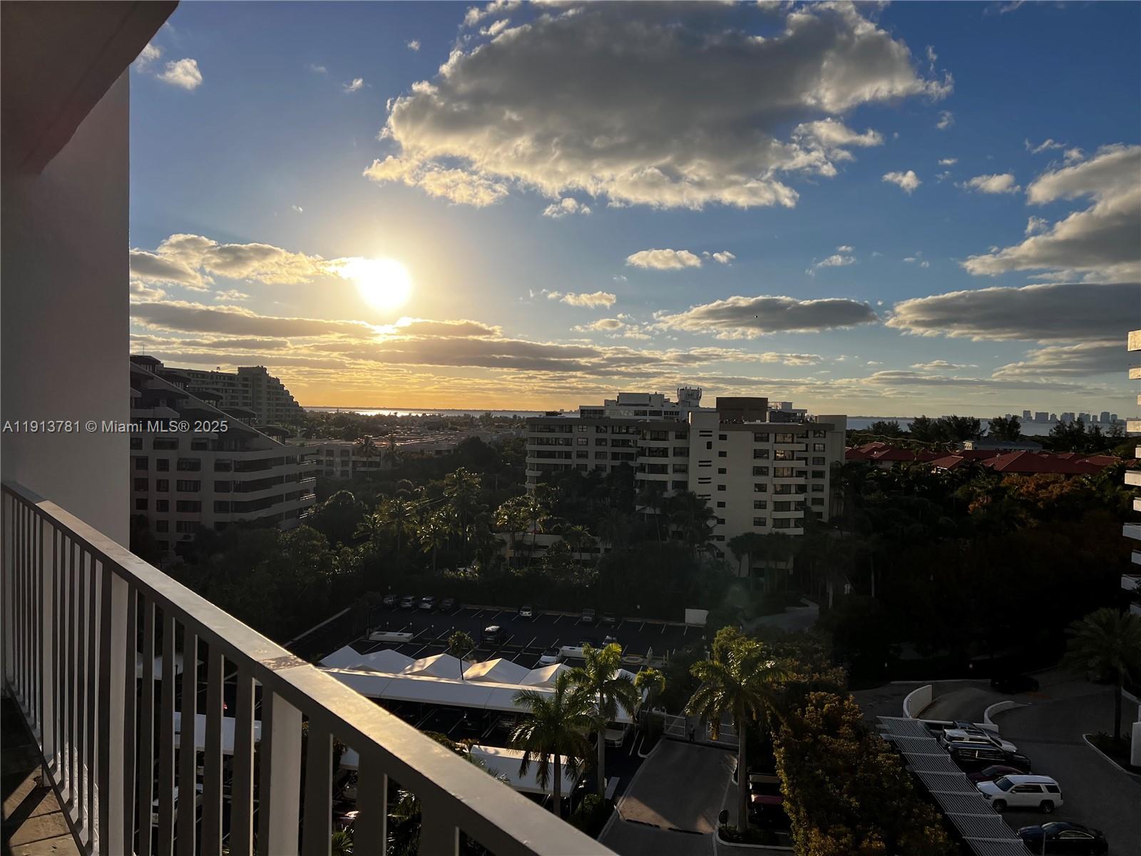 A balcony view overlooks a parking lot, palm trees, and apartment buildings at sunset — 200 Ocean Lane Dr # 909, Key Biscayne FL 33149, KEY BISCAYNE, FL
