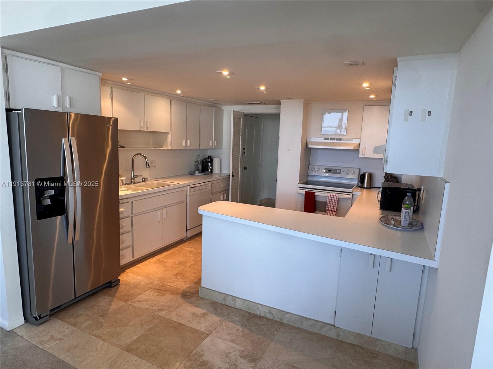 A kitchen features white cabinetry, stainless steel appliances, a breakfast bar, and tiled flooring — 200 Ocean Lane Dr # 909, Key Biscayne FL 33149, KEY BISCAYNE, FL