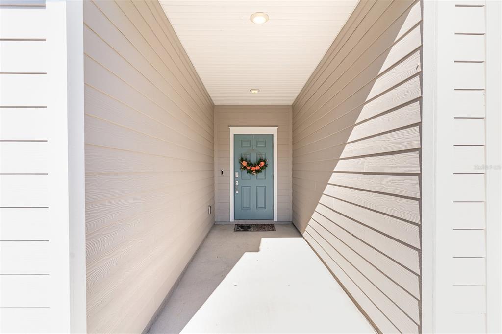 A covered entryway features light-colored horizontal siding, a concrete floor, and a blue front door — 710 NW 126TH TERRACE, NEWBERRY, FL
