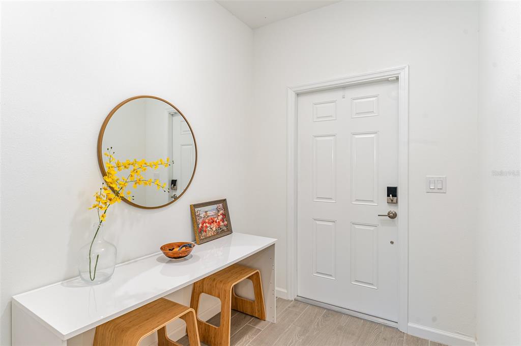 A white entryway features a console table, two wooden stools, a round mirror, and a door — 710 NW 126TH TERRACE, NEWBERRY, FL