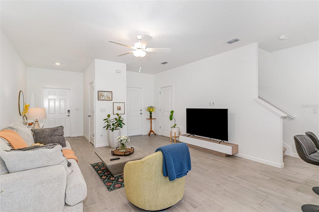 A living room features light tile flooring, a ceiling fan, a television, and a staircase — 710 NW 126TH TERRACE, NEWBERRY, FL