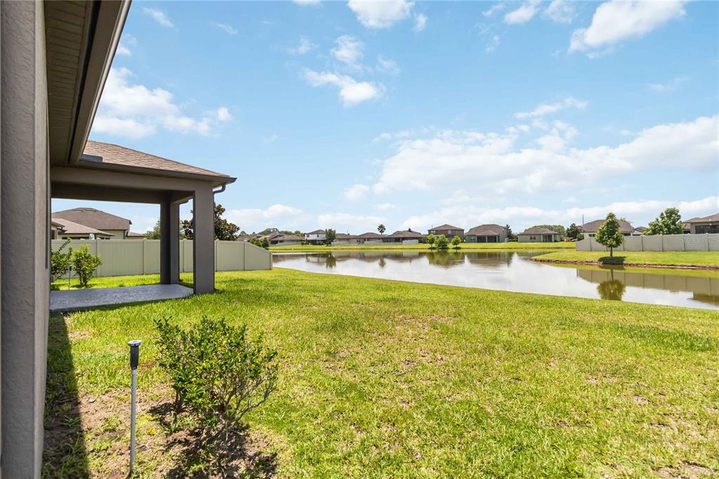A backyard view featuring a covered patio, a grassy lawn, and a pond — 3900 BAJA DRIVE, ST CLOUD, FL