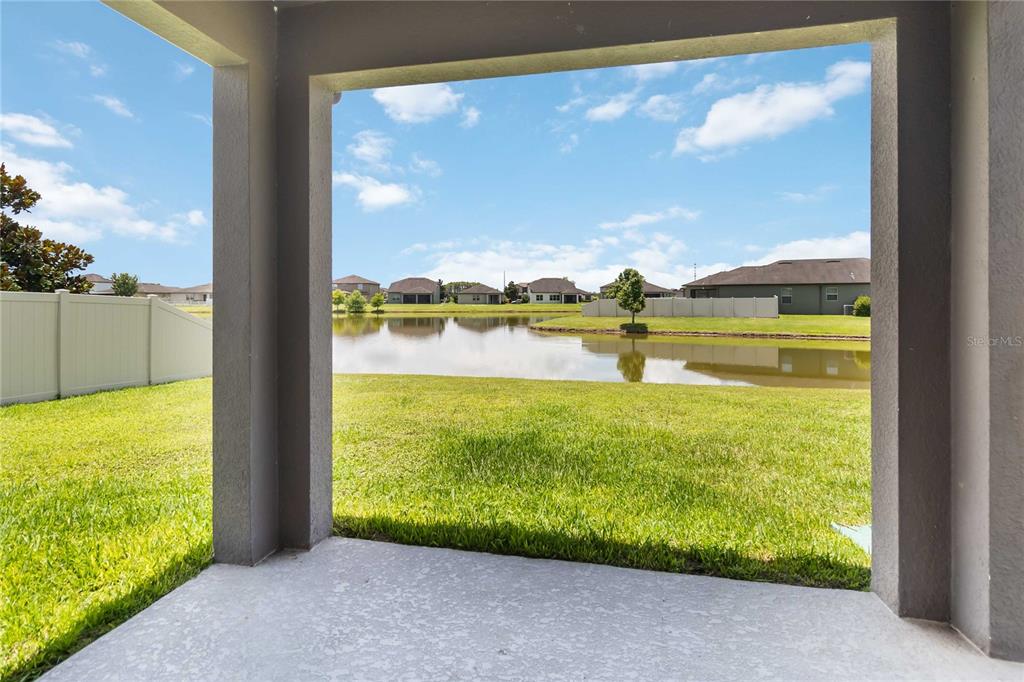 A covered concrete patio overlooks a grassy backyard and a small pond with houses beyond — 3900 BAJA DRIVE, ST CLOUD, FL
