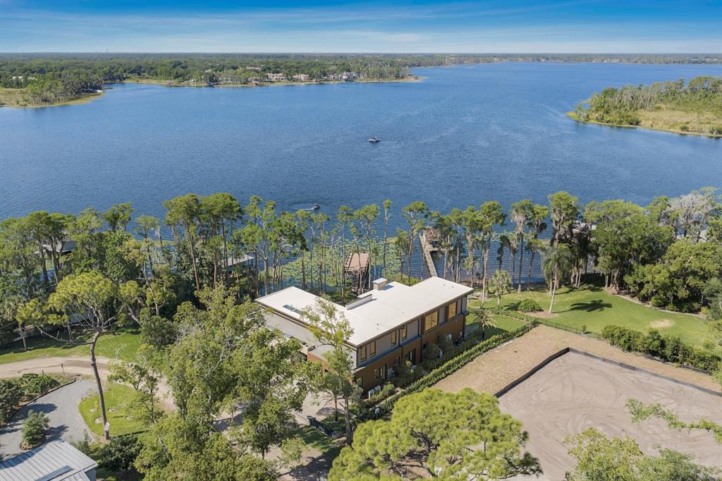 An aerial view shows a modern house situated on a lakefront lot with trees — 728 FOREST STREET, WINDERMERE, FL