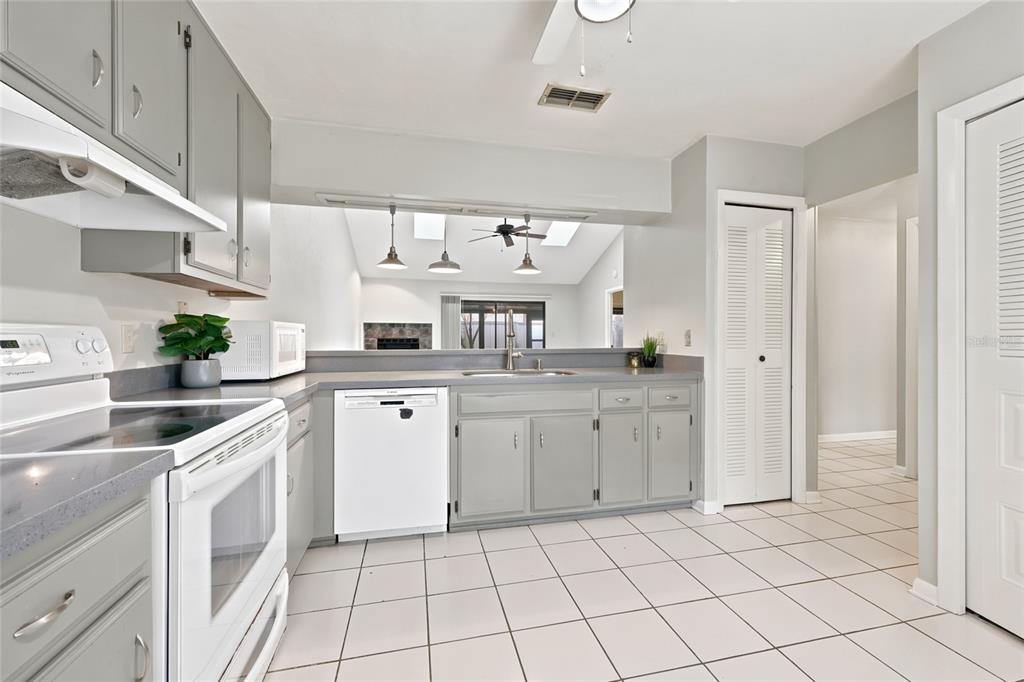 A kitchen with gray cabinets, white appliances, and tiled floors overlooks an adjacent living area — 3711 NW 56TH LANE, GAINESVILLE, FL