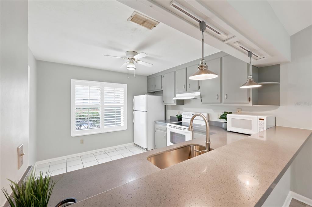 A kitchen features gray cabinets, a stainless steel sink, quartz countertops, and white appliances — 3711 NW 56TH LANE, GAINESVILLE, FL