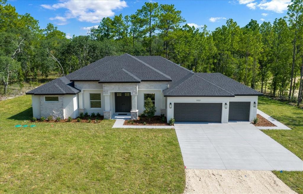 A single-story house with a white stone facade, dark roof, and a three-car garage — 11021 STILT AVENUE, WEEKI WACHEE, FL