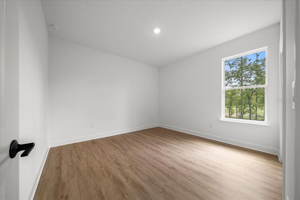 An empty bedroom with white walls, light wood-look flooring, and a window overlooking trees — 11021 STILT AVENUE, WEEKI WACHEE, FL