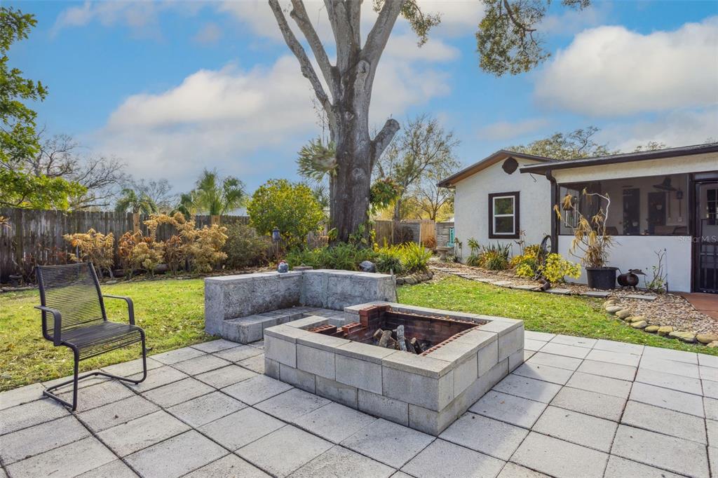 A backyard patio features a square stone fire pit, a built-in bench, and a chair — 1023 N BASK DRIVE, TAMPA, FL