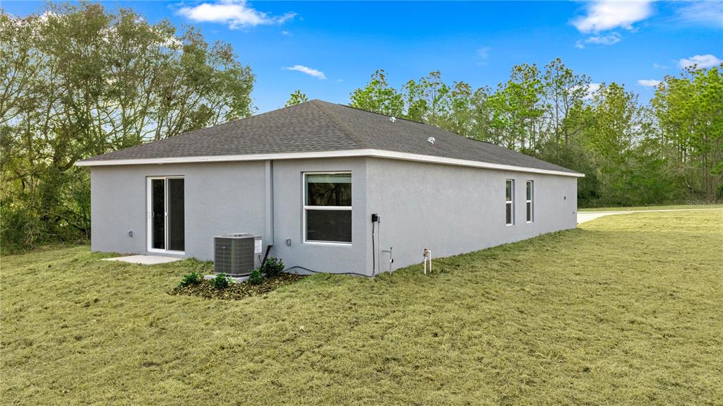 The exterior rear view of a gray stucco house features a sliding glass door and AC unit — 8099 SW 45TH COURT, OCALA, FL