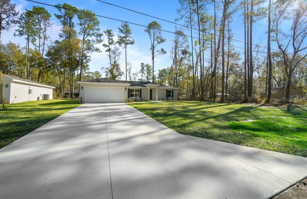 A single-story house with a white garage and driveway sits on a grassy, wooded lot — 9927 N ATHENIA DRIVE, CITRUS SPRINGS, FL
