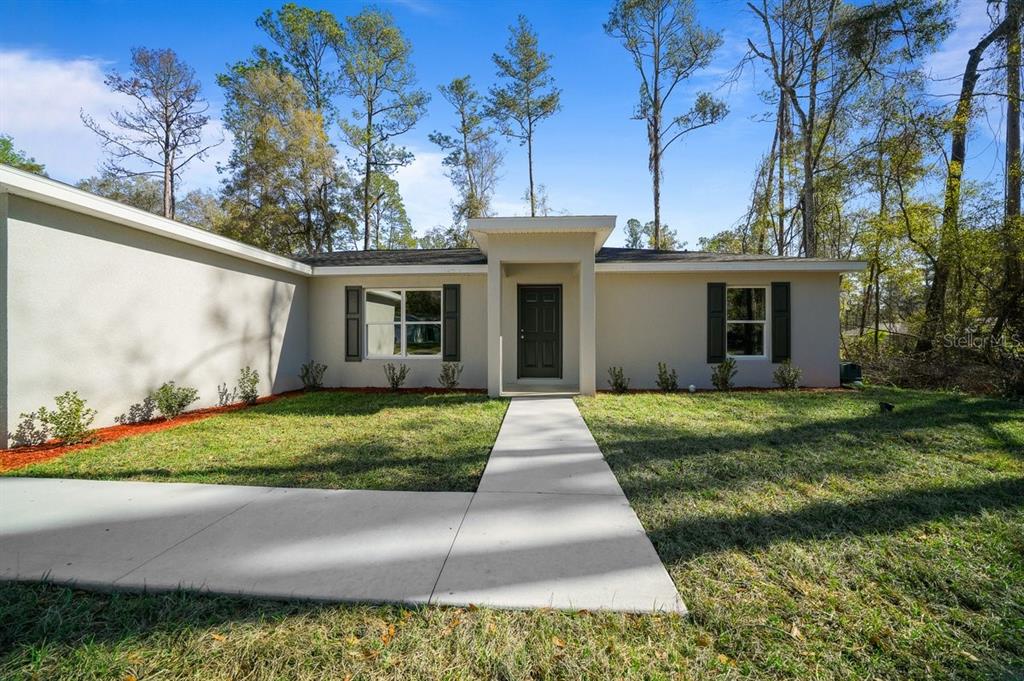 A single-story house with a light-colored exterior, dark shutters, and a concrete walkway — 9927 N ATHENIA DRIVE, CITRUS SPRINGS, FL