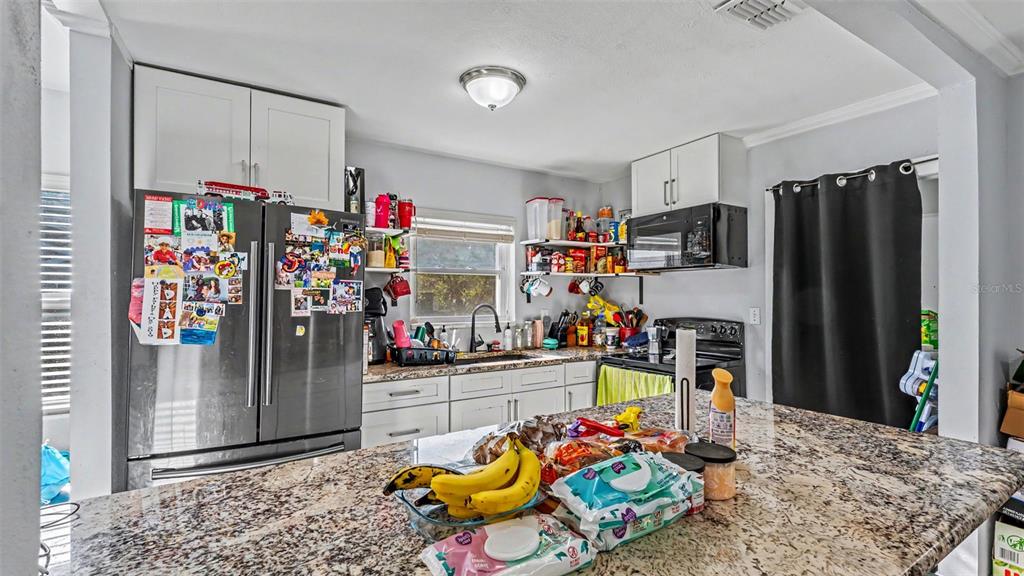 A kitchen features granite countertops, white cabinetry, a stainless steel refrigerator, and a black curtain — 861 E LOWELL STREET, LAKELAND, FL