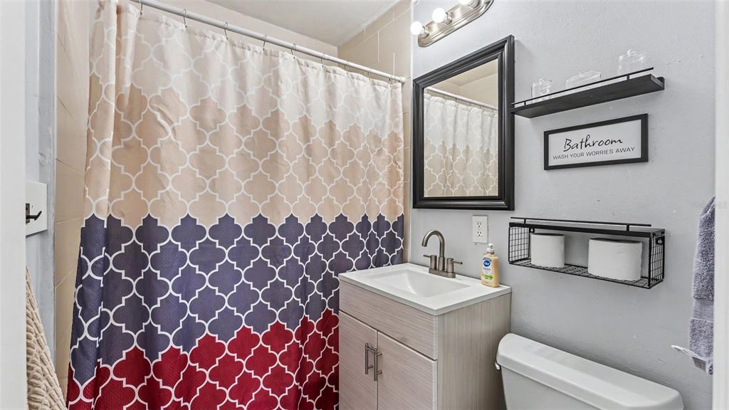 A small bathroom features a patterned shower curtain, a vanity, and wall-mounted storage shelves — 861 E LOWELL STREET, LAKELAND, FL