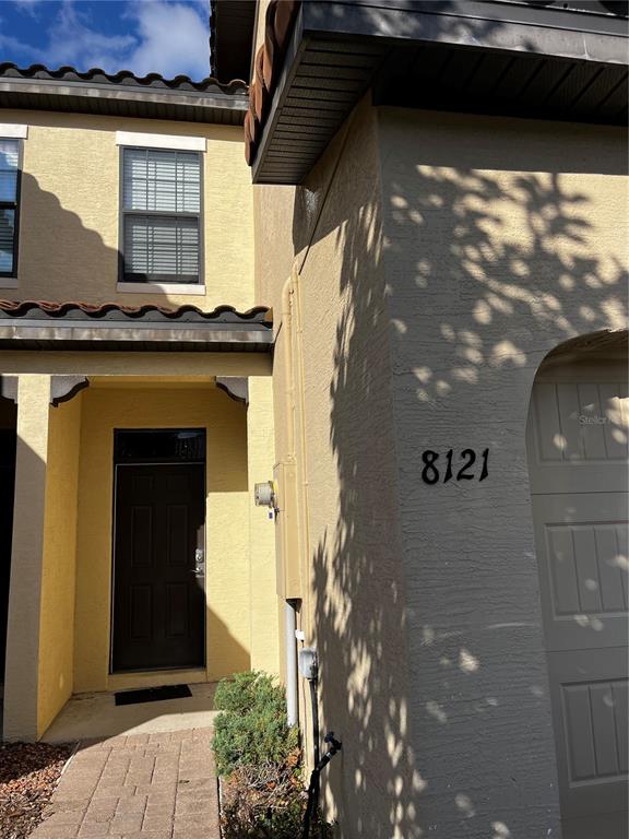 The exterior of a tan stucco townhouse features a dark front door and garage entrance — 8121 ROSEVILLE BOULEVARD, DAVENPORT, FL