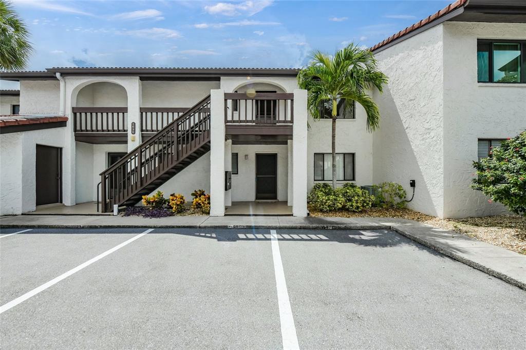 A two-story apartment building exterior features a brown wooden staircase and a parking lot — 1630 STICKNEY POINT ROAD UNIT 101, SARASOTA, FL