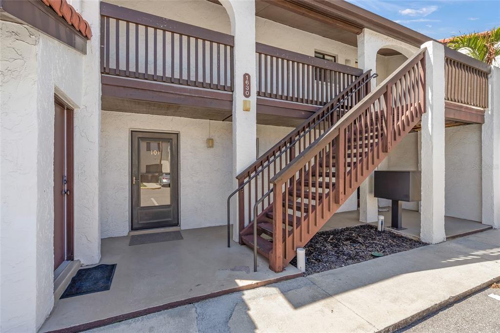 An exterior view of a two-story building with a wooden staircase and a ground-floor entrance — 1630 STICKNEY POINT ROAD UNIT 101, SARASOTA, FL